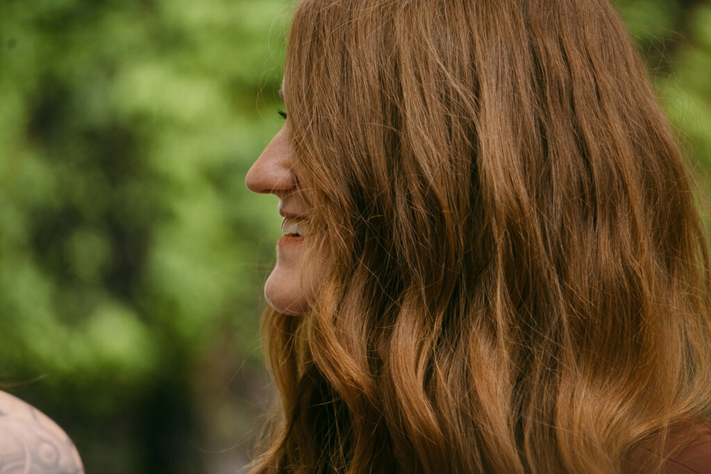 Close up of a bride grinning during her ceremony, with a cascade of red curls of hair over her face.