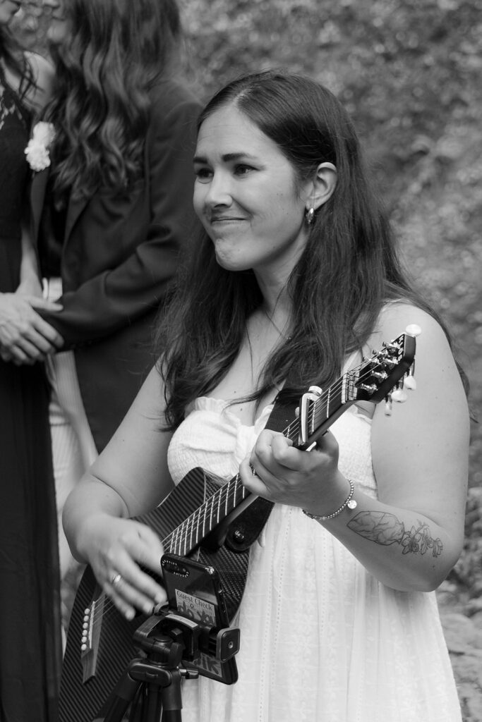 Black and white image of a woman in a white dress playing a ukulele at the Wahclalla Falls elopement in Oreogn.