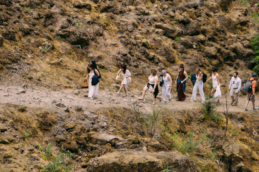 Elopement guests clad in white hike along the trail that leads to the ceremony location.