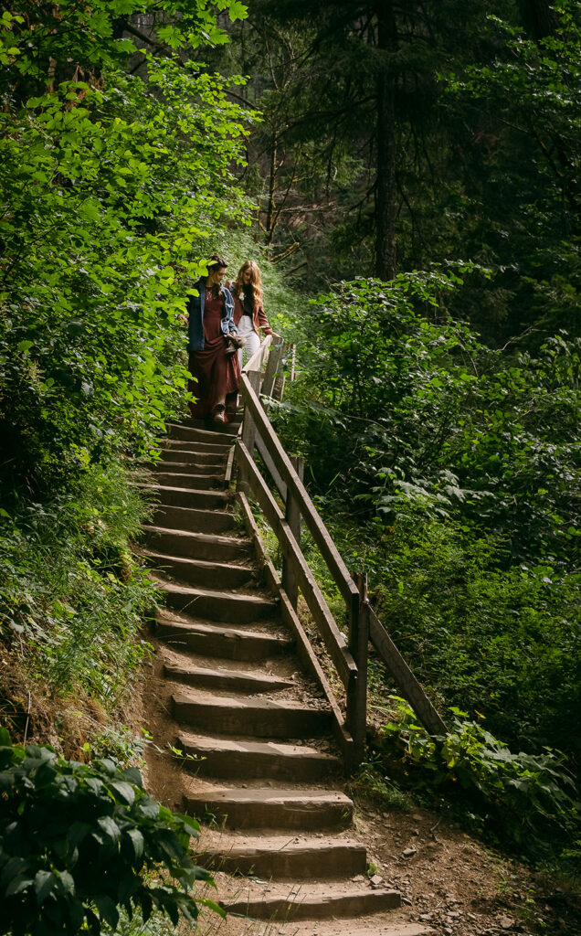 the two brides descend a staircase along the trail in the forest together, while hiking out after their elopement ceremony.