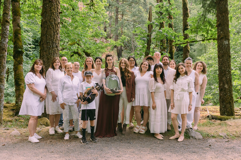 The entire group of guests and the two brides pose for a photo together in the forest after the elopement ceremony.
